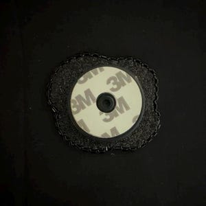 May include: A circular phone grip with a 3M adhesive backing. The grip is white with the 3M logo printed on it. It is surrounded by a black, textured border. The grip is designed to attach to the back of a phone.