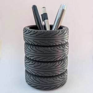 May include: A black tyre-shaped desk organiser with five stacked tyres. The organiser is filled with pens and pencils.