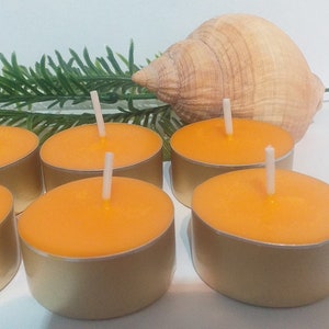 May include: Six orange tea light candles in gold metal containers. The candles are arranged in a semi-circle on a white surface.