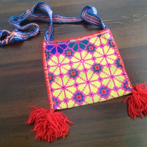 May include: A small, colorful, embroidered bag with a geometric pattern in shades of pink, yellow, blue, and green. The bag has a long strap and red tassels.