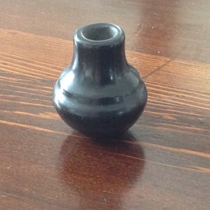 May include: A small, black, ceramic pot with a rounded base and a slightly flared opening. The pot has a smooth, glossy finish.