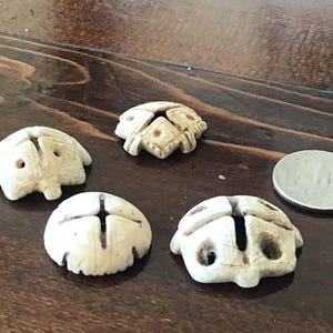 May include: Five small, off-white carved objects, possibly beads or decorative elements, are arranged on a dark wooden surface. One coin is also present. The objects have a unique, textured appearance.