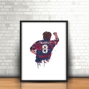 Peut inclure: Une peinture à l'aquarelle d'un joueur de football portant un maillot rouge, blanc et bleu avec le nom "BEARDSLEY" et le numéro "8" au dos. Le joueur est tourné dos au spectateur et a le bras levé en l'air.