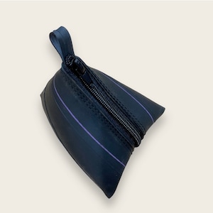 Può includere: Una piccola pochette nera con cerniera realizzata con camere d'aria per biciclette riciclate. La pochette ha una striscia viola che corre al centro.
