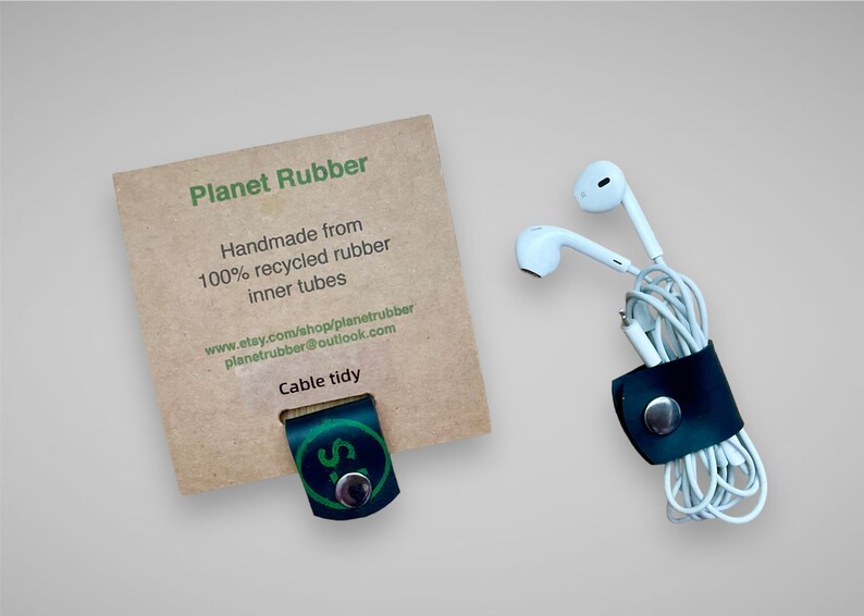 May include: A black leather cable tidy with a silver button, handmade from 100% recycled rubber inner tubes. The tidy is holding a pair of white earbuds. The packaging includes the text "Planet Rubber", "Handmade from 100% recycled rubber inner tubes", "www.etsy.com/shop/planetrubber", "planetrubber@outlook.com", and "Cable tidy".