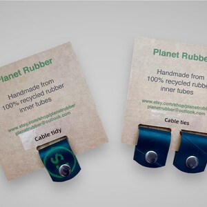 May include: Two brown cardboard cards with the text "Planet Rubber" and information about the product. The cards are displaying two black rubber cable ties.