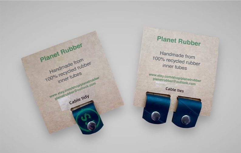 May include: Two brown cardboard cards with the text "Planet Rubber" and information about the product. The cards are displaying two black rubber cable ties.
