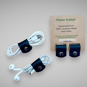 May include: Three black leather cable ties made from 100% recycled inner tubes. The cable ties are shown holding together various cords and wires. The text on the card reads "Planet Rubber Handmade from 100% recycled rubber inner tubes www.etsy.com/shop/planetrubber planetrubber@outlook.com Cable ties"
