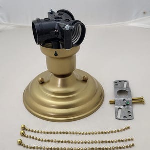 May include: A gold-colored ceiling light fixture with a black light socket. Includes a mounting bracket, screws, and three gold-colored pull chains. The fixture has a round base with decorative details.