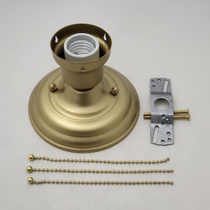 Op de afbeelding: Een goudkleurige plafondlamp met een lamphouder, montagebeugel en drie kralenkettingen. De lamp heeft een ronde basis en een cilindrische lamphouder. De montagebeugel is zilverkleurig met twee schroeven.