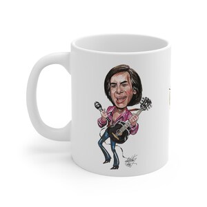 May include: White ceramic mug with a cartoon illustration of a musician playing a guitar and singing into a microphone. The illustration is in bright colours, with the musician wearing a pink shirt and blue trousers. The mug has a curved handle.
