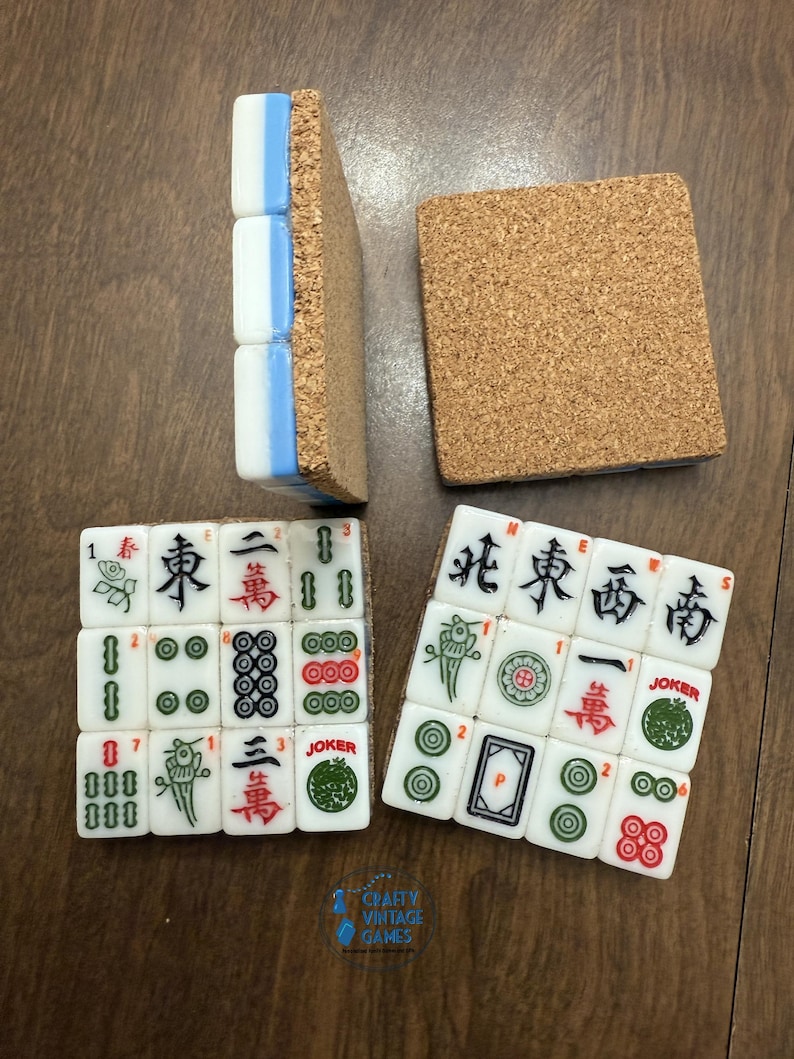 May include: Four square coasters crafted from white Mahjong tiles with blue sides and cork backings. Two coasters are face-up, displaying various Mahjong characters, symbols, and Joker tiles in red, green, and black ink. One coaster is flipped to show the cork base.