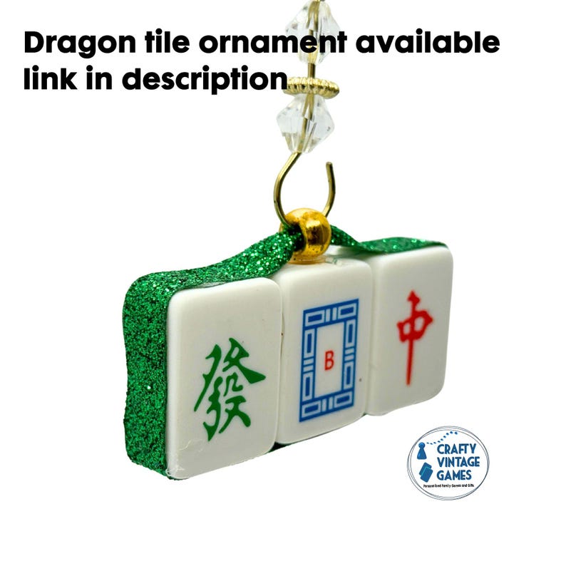 Puede incluir: Un adorno de azulejo de drag&oacute;n con tres azulejos blancos con s&iacute;mbolos verdes, azules y rojos. Los azulejos est&aacute;n conectados con una cinta de purpurina verde y herrajes dorados. El texto "Dragon tile ornament available link in description" est&aacute; en la parte superior.