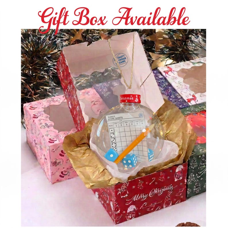 May include: A clear, spherical Christmas ornament containing a Bunco score sheet, a yellow pencil, and two blue dice. The ornament has a red cap and is nestled in gold tissue paper inside a red box with white holiday patterns and text.