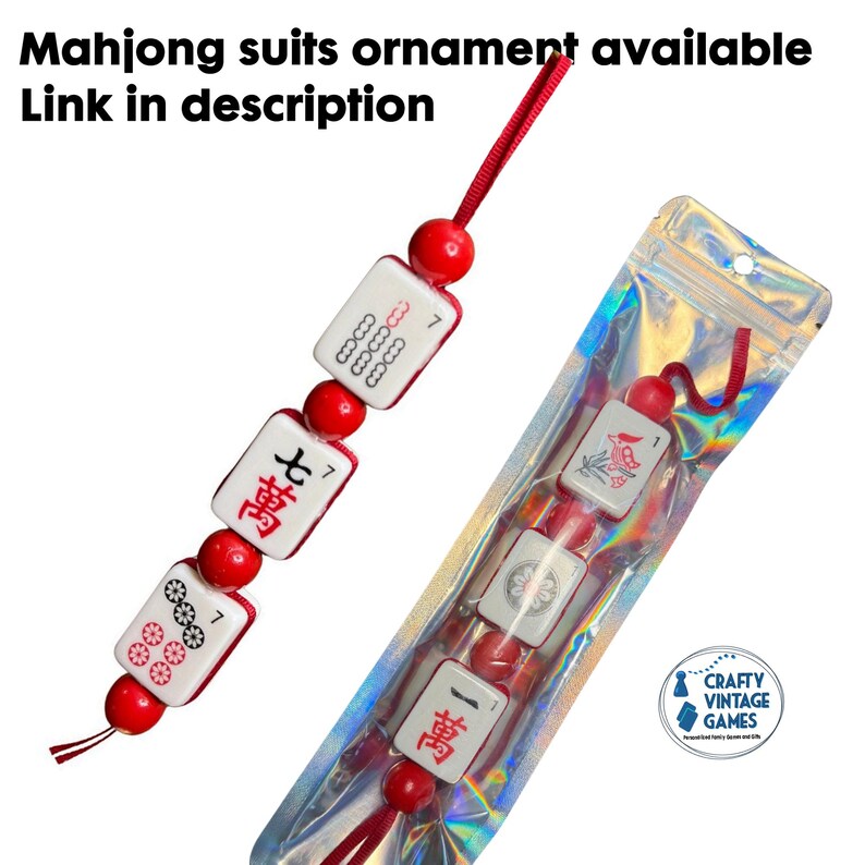 Puede incluir: Un adorno de fichas de Mahjong rojas y blancas, con cuentas rojas y una cuerda roja. Otro adorno similar es visible dentro de una bolsa de pl&aacute;stico sellada. El texto "Mahjong suits ornament available" y "Link in description" est&aacute; en la parte superior.