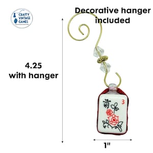 Puede incluir: Adorno decorativo de ficha de Mahjong con un colgador dorado. La ficha es blanca con dise&ntilde;os florales rojos y el n&uacute;mero 3. El adorno mide 10,8 cm con el colgador y 2,5 cm de ancho.