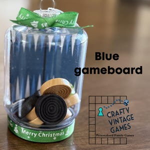 May include: A clear plastic ornament with a blue and white game board inside. The ornament is decorated with green ribbon and the words "Merry Christmas". The ornament is labeled "Blue gameboard" and "Crafty Vintage Games".