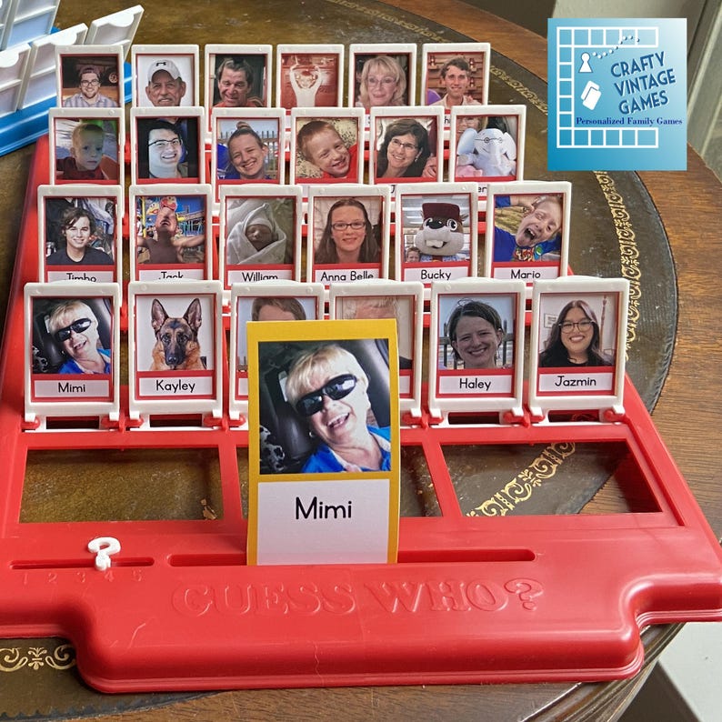 Może przedstawiać: Czerwono-biała plansza do gry Guess Who? z r&oacute;żnymi zdjęciami os&oacute;b i psa. Plansza do gry ma mechanizm przesuwny do ujawniania zdjęć. Plansza do gry znajduje się na drewnianym stole.
