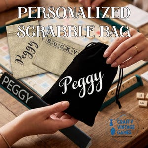 May include: A black drawstring bag featuring the name Peggy in white script lettering. The bag is made of fabric and includes a black cord closure. The design is displayed alongside other fabric bags with personalised text and game tiles.