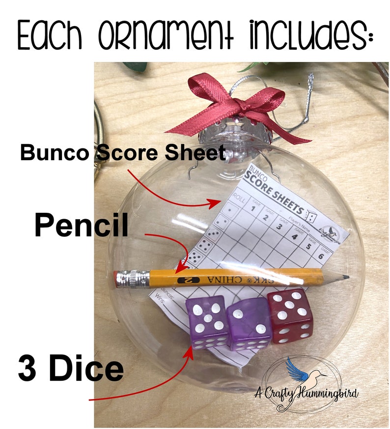 May include: A clear, spherical glass ornament topped with a red ribbon bow. Inside the ornament are a Bunco score sheet, a yellow pencil with a metal ferrule and eraser, and three six-sided dice in purple, light purple, and red colors.
