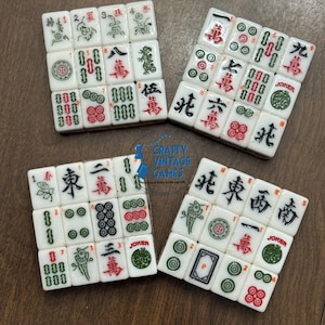 May include: Four square arrangements of white Mahjong tiles featuring various red, green, and black engraved symbols, characters, and numbers. Each tile displays distinct traditional markings including bamboo, circles, winds, dragons, and joker labels.