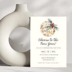 May include: A New Year's Eve invitation card with a gold glitter ball illustration, adorned with green sprigs and red berries. The text reads "Cheers to the New Year!" and includes event details.