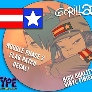 May include: A round decal featuring a cartoon image of Noodle from Gorillaz, with text that reads "NOODLE PHASE 2 FLAG PATCH DECAL!" and "HIGH QUALITY VINYL FINISH!". The decal includes a flag design with red, white, and blue colors. The graphic is from Type Graphic Studio.