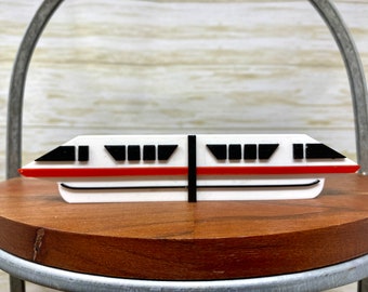May include: A white and red model of a monorail train with black windows. The model is made of plastic and is about 15 cm long.