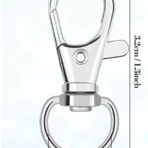May include: A silver-colored metal lobster claw clasp with a swivel base and a circular ring attachment. The clasp measures 1.3 inches in total length, and the circular ring has a diameter of 0.4 inches as indicated by the visible measurement lines.