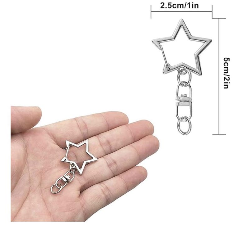 Pode incluir: Chaveiro prateado em forma de estrela com fecho mosquet&atilde;o e argola. A estrela mede 2,5 cm de largura e 5 cm de comprimento. O chaveiro &eacute; mostrado na m&atilde;o de uma pessoa.