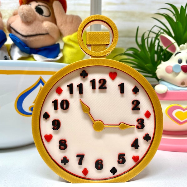 May include: A gold-coloured pocket watch with a white face and black numbers. The watch face has red hearts, diamonds, and spades around the edge. The hands are gold-coloured.