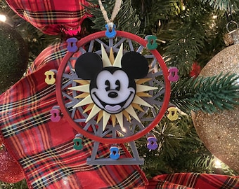 Könnte beinhalten: Ein roter, weißer und gelber Weihnachtsbaumschmuck mit dem Gesicht von Mickey Mouse in der Mitte eines Riesenrads. Der Schmuck ist mit bunten Mickey Mouse-Symbolen verziert.