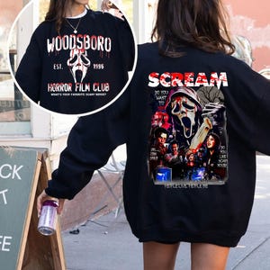 May include: Black sweatshirt with "WOODSBORO" and a ghost face graphic. The front of the sweatshirt has "HORROR FILM CLUB" text. The back features "SCREAM" text and a movie poster graphic with the text "DO YOU WANT TO" and "PEOPLE LIVE, PEOPLE DIE".
