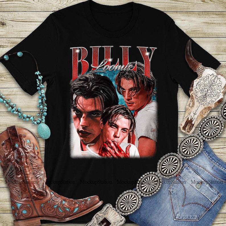 Puede incluir: Camiseta negra con un gr&aacute;fico vintage de tres hombres y el texto "BILLY LOOMIS" en rojo. La imagen se muestra con un collar turquesa, una bota de vaquero marr&oacute;n y un cintur&oacute;n plateado.