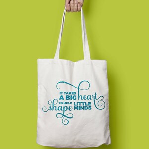 Puede incluir: Bolsa de tela blanca con texto azul que dice "Se necesita un gran coraz&oacute;n para ayudar a moldear las mentes peque&ntilde;as".
