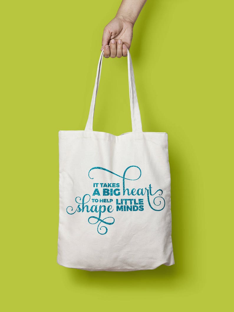 Puede incluir: Bolsa de tela blanca con texto azul que dice "Se necesita un gran coraz&oacute;n para ayudar a moldear las mentes peque&ntilde;as".