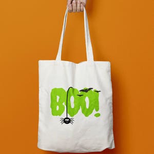May include: White canvas tote bag with a green "BOO!" graphic and a black spider hanging from the "O". There are also black bats flying above the text.