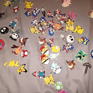 May include: A collection of colorful metal charms featuring popular video game characters, including Pikachu, Mario, Sonic the Hedgehog, and Minecraft characters. The charms are perfect for adding a touch of fun to keychains, bracelets, or other accessories.