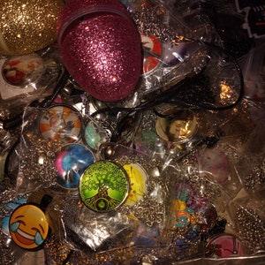 May include: A variety of colorful necklaces with different pendants, including a tree of life pendant, a smiley face pendant, and a galaxy pendant. The necklaces are packaged in clear plastic bags and are displayed on a table.