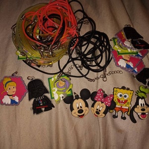 May include: A collection of colorful character necklaces featuring popular cartoon characters like Mickey Mouse, Spongebob Squarepants, and Darth Vader. The necklaces are made of black and neon yellow cord and come with a variety of colorful character charms.