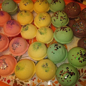 May include: A collection of colorful bath bombs with glitter. The bath bombs are arranged in a circle on a plate with a fall-themed design.