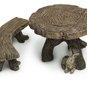 May include: A miniature wooden table and two benches set. The table is made from a tree trunk slice and has three legs. The benches are curved and have three legs each. A small white rabbit figurine is sitting under the table.