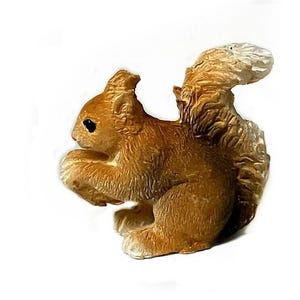 May include: A small, brown squirrel figurine with a bushy tail. The squirrel is sitting on its haunches with its paws tucked in front of it.
