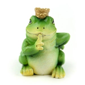 Op de afbeelding: Een groene kikkerfiguur met een gouden kroon, met zijn vinger op zijn lippen, alsof hij 'ssst' zegt.