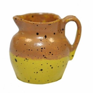 May include: A small, brown and yellow ceramic pitcher with black speckles. The pitcher has a rounded body and a handle.