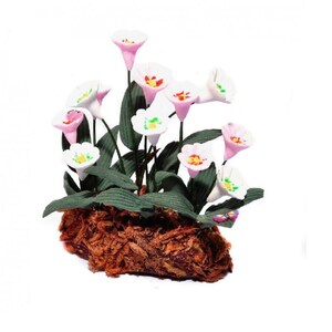 Puede incluir: Un pequeño arreglo de flores blancas y rosas con hojas verdes, colocado en una base marrón texturizada. Las flores están hechas de tela y tienen un aspecto delicado y realista.