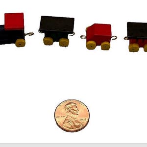 Könnte beinhalten: Ein Miniatur-Holzzugset mit einer schwarzen Lokomotive und einem roten Schlusslicht. Die Waggons haben gelbe Räder und sind durch silberne Kupplungen verbunden. Der Zug ist etwa so groß wie ein 1-Cent-Stück.