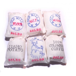 May include: A collection of small, off-white burlap sacks, each labeled with various food items and weights. The sacks are printed with text such as "Flour," "Salt," "Sugar," "Idaho Potato," "Fertilizer," and "100% Colombia Coffee." Each sack is marked with "50 LBS."