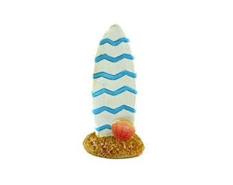 May include: A white surfboard with blue chevron stripes and a pink seashell at the bottom. The surfboard is sitting on a brown base that looks like sand.