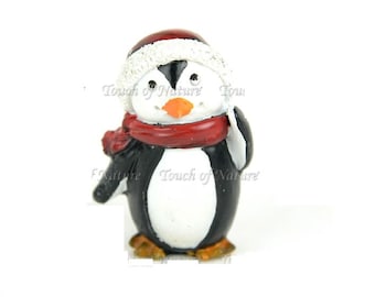 May include: A small penguin figurine wearing a red and white Santa hat and a red scarf. The penguin is black and white with a bright orange beak.